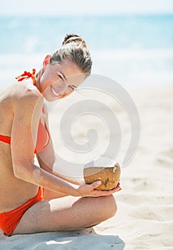 Smiling young woman sitting on beach with coconut