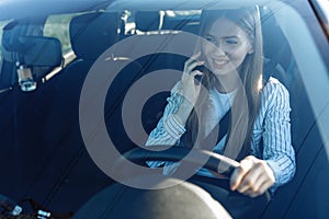 Smiling young woman sitting in car talking on mobile phone while driving