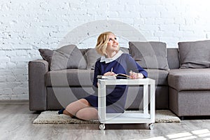 Smiling young woman sitting on the carpet with her notebook