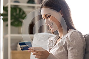 Smiling young woman sitting on coach holding credit card