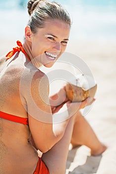 Smiling young woman sitting with coconut on beach