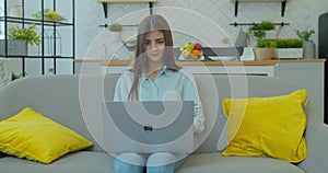 Smiling young woman sitting on couch using laptop notebook looking at screen typing message, happy lady chatting on