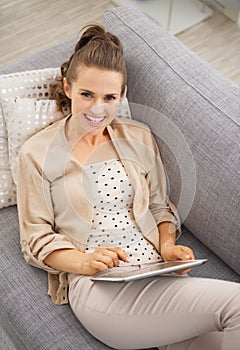 Smiling young woman sitting on divan and using tablet pc