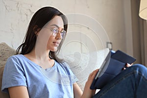 Smiling young woman sitting on sofa with digital tablet and chating with friends.