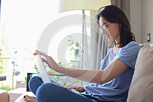 Smiling young woman sitting on sofa with laptop computer and chating with friends.