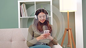 Smiling young woman sitting on a sofa looking at social media with a smartphone