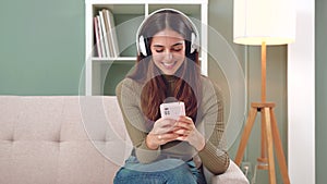 Smiling young woman sitting on a sofa looking at social media with a smartphone