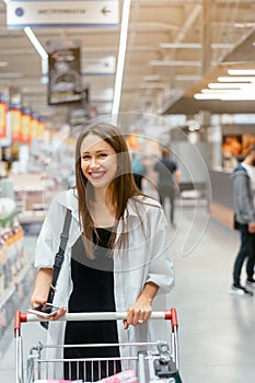 Smiling young woman with smartphone in supermarket