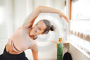 Smiling young woman in sports clothing doing side bending exercise at home