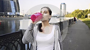 Smiling young woman in a sportswear drinking water and walking in Moscow city