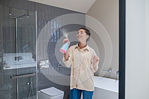 A smiling young woman spraying the air freshener in the bathroom