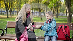 Smiling young woman spraying sanitizer on hands of cute Caucasian boy sitting on bench in autumn park. Caucasian family
