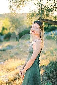 Smiling young woman stands half-turned near a tree