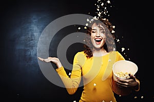 Smiling young woman staying under popcorn shower with right hand up