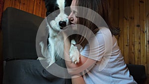 Smiling young woman stroking playing with cute puppy dog border collie on couch sofa at home indoor. Owner girl with pet