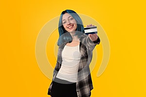 Smiling young woman student with blue hair holding a credit card