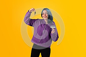 Smiling young woman student with blue hair holds a credit card and key