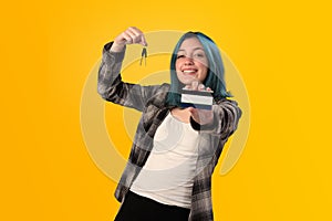 Smiling young woman student with blue hair holds a credit card and key