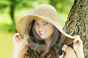 Smiling young woman in sun hat against background of summer green park. Beautiful healthy happy girl enjoying freedom