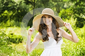 Smiling young woman in sun hat against background of summer green park. Beautiful healthy happy girl enjoying freedom outside