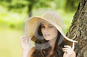 Smiling young woman in sun hat against background of summer green park. Beautiful healthy happy girl enjoying freedom outside