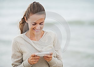 Smiling young woman in sweater on beach writing sms