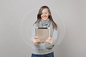 Smiling young woman in sweater, scarf using tablet pc computer, making video call isolated on grey background. Healthy