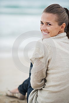 Smiling young woman in sweater sitting on lonely beach