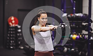 Smiling young woman swinging a dumbbell at the gym