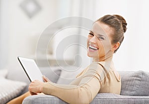 Smiling young woman with tablet pc sitting on sofa