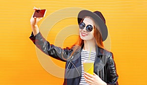 smiling young woman taking selfie picture by phone with cup of juice over orange wall background