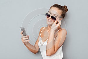 Smiling young woman talking on mobile phone and holding sunglasses