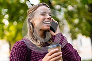 Smiling young woman talking phone on summer street drinking coffee outdoor