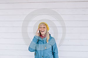 Smiling young woman talking on the phone. woman in yellow knitted hat and a blue jacket using cell phone