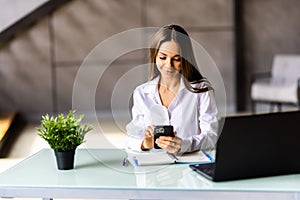 Smiling young woman with titled head leaned on her hand sitting at her office desk