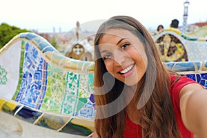 Smiling young woman tourist taking selfie self portrait sitting on the bench decorated with mosaic in famous Park Guell, Barcelona