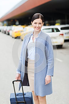 Smiling young woman with travel bag over taxi