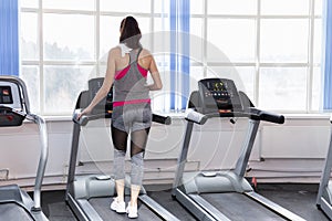 Smiling young woman on a treadmill in the gym. Active lifestyle and health. Back view