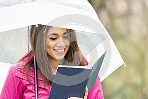 Smiling young woman with umbrella reads book in the park.
