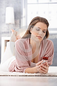 Smiling young woman using cellphone on floor