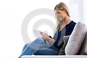 Smiling young woman using her digital tablet while sitting on sofa at home.