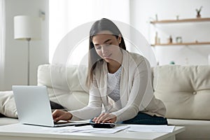 Smiling young woman using laptop and calculator, checking finances