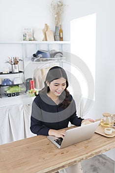 Smiling young woman using laptop in the kitchen at home photo