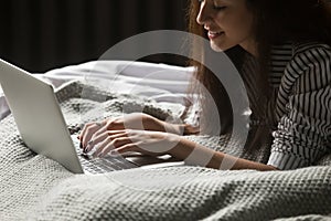 Smiling young woman using laptop lying on bed, close up