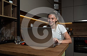Smiling young woman using laptop, sitting on chair at home, beautiful girl shopping or chatting online in social network, having f