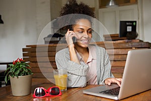 Smiling young woman using laptop and talking on mobile phone