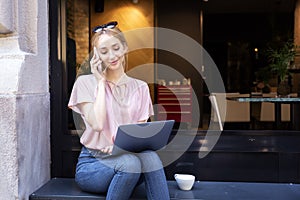 Smiling young woman using mobile phone and laptop while sitting in the cafe