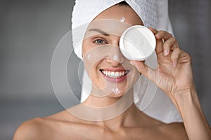 Smiling young woman using moisturizing face cream in bathroom