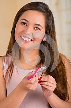 Smiling young woman using a shaver on her hair, bath background