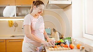 Smiling young woman waiting for baby cooking on kitchen and doing housework. Concept of healthy lifestyle and nutrition